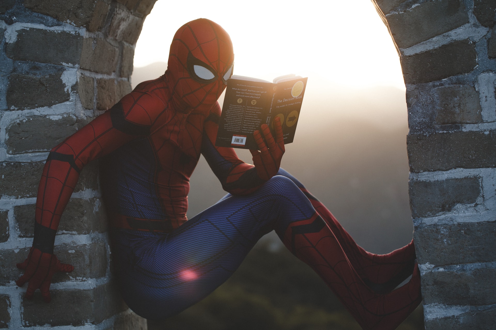 El superhéroe Spiderman sentado en una torre de piedra leyendo un libro